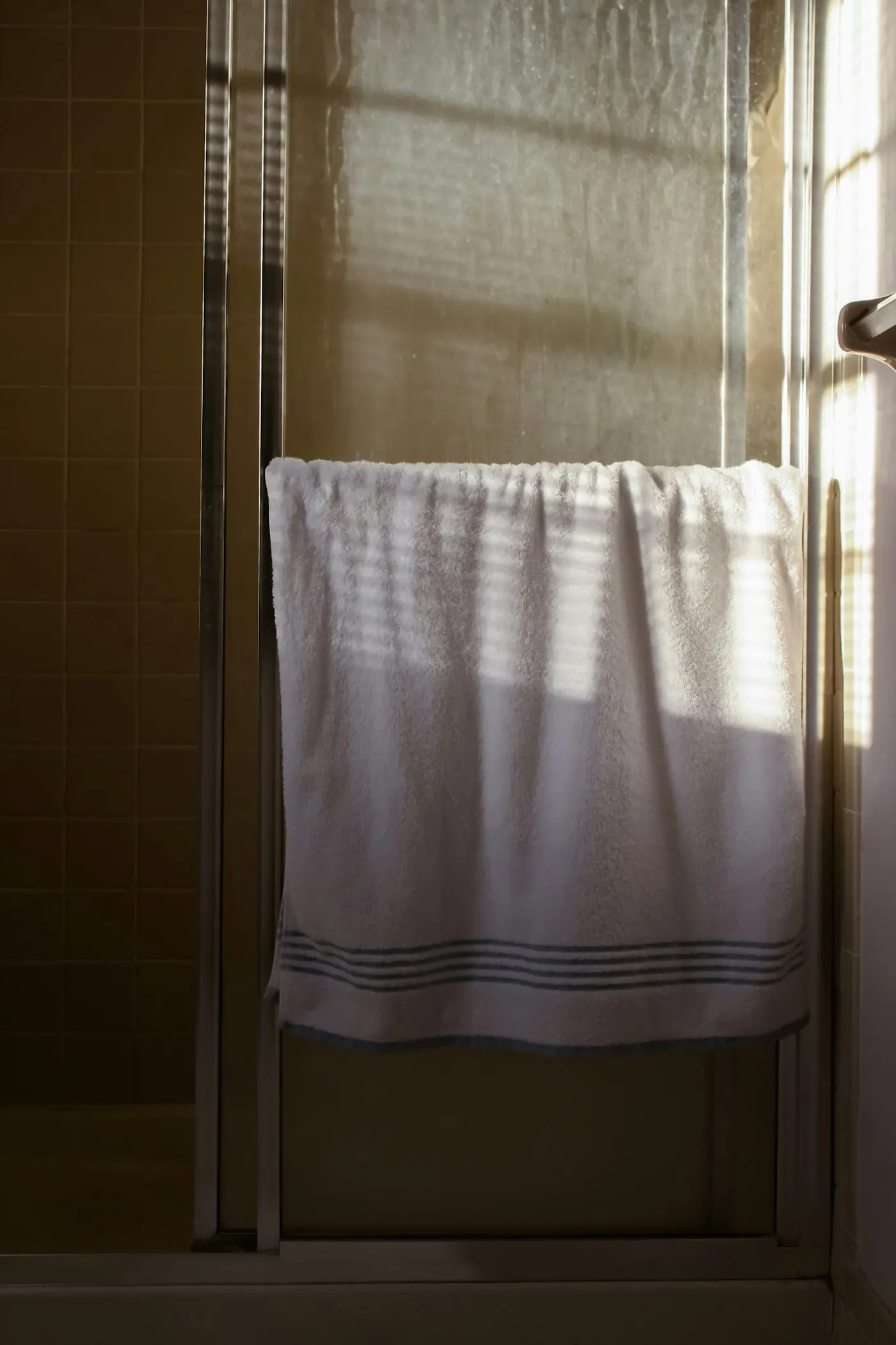 White towel hanging from a metal towel rail in warm daylight