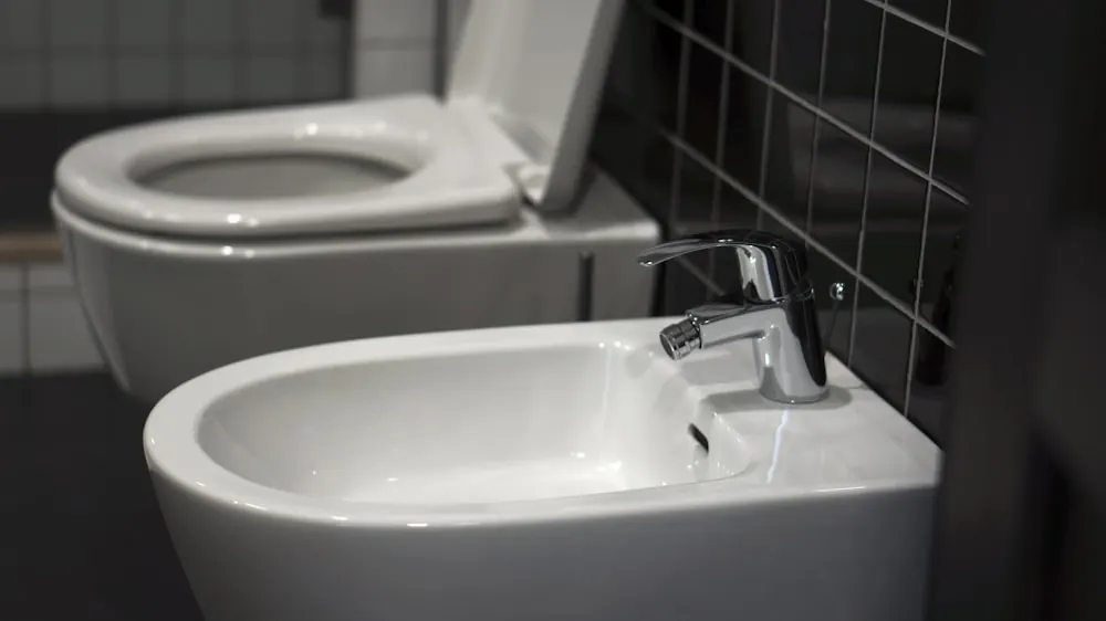 White ceramic bidet with a chrome mixer tap installed beside a wall-hung toilet