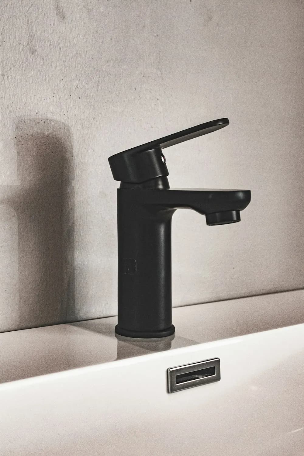 Matte black single-lever basin mixer tap mounted on a white washbasin against a plain wall