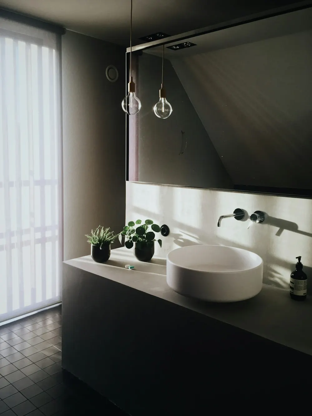 Round countertop washbasin with a wall-mounted mixer tap on a dark vanity beside a window
