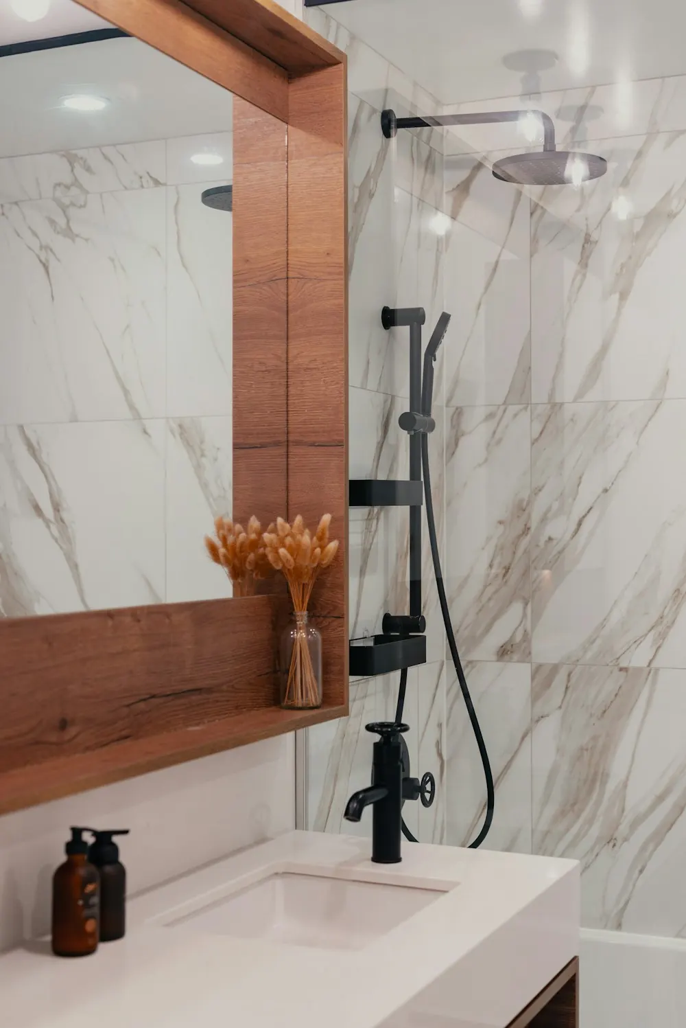 Marble-tiled bathroom detail with a framed mirror, matte black shower fittings and a washbasin
